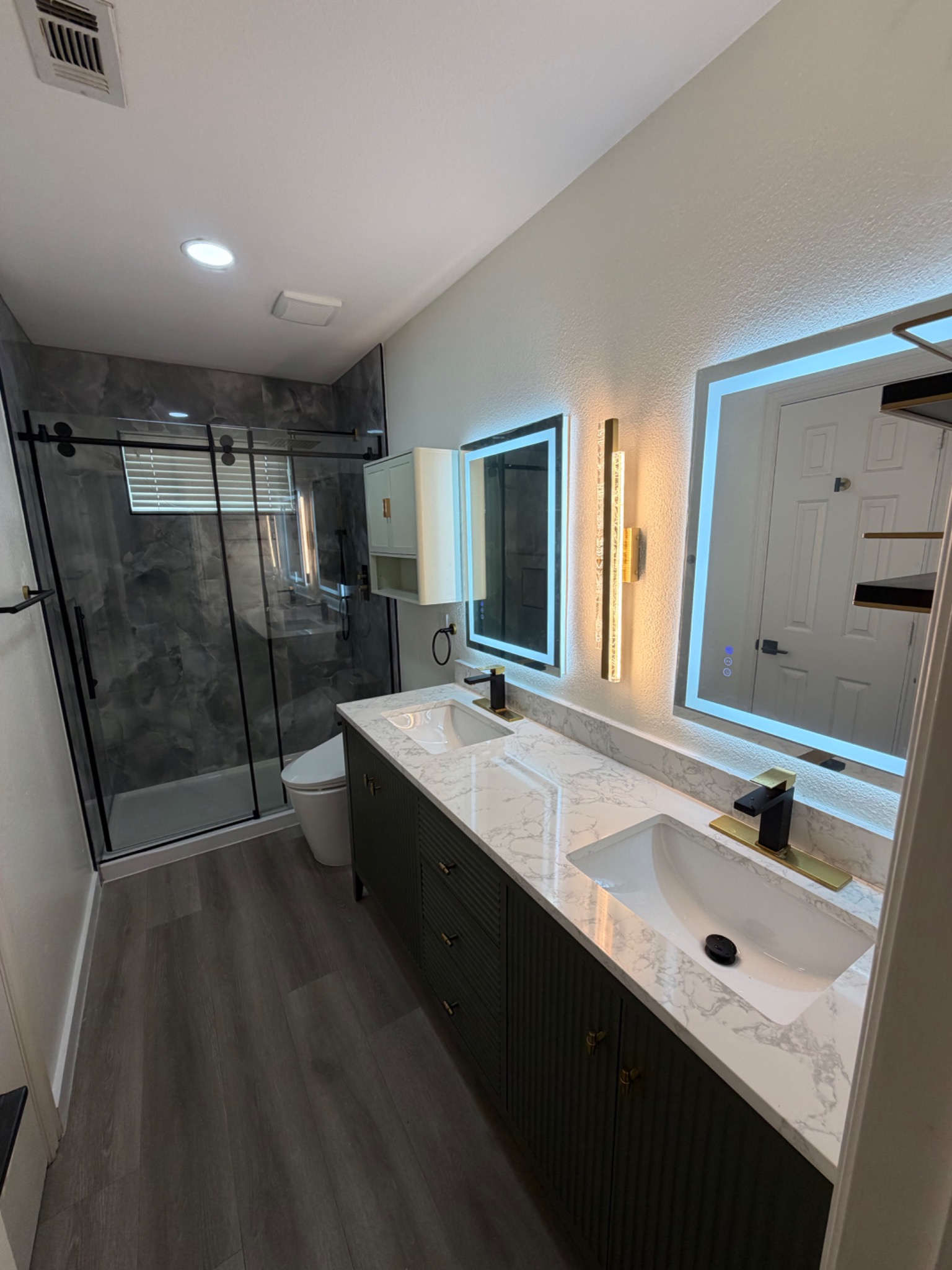 Bathroom with a glass shower, dark double vanity, marble-pattern countertop and illuminated mirrors